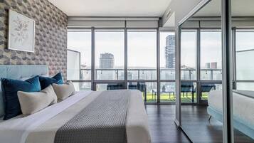 A modern bedroom with a large bed, a city view through floor-to-ceiling windows, and a patterned wall.