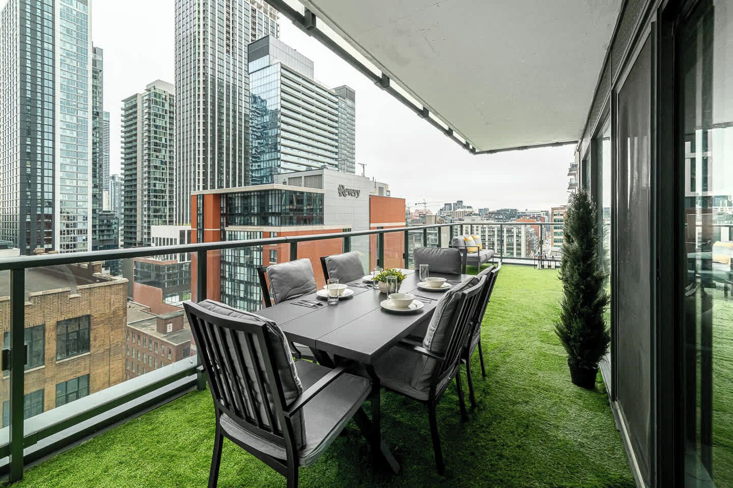Un balcon avec une table et des chaises pour prendre les repas, une petite plante en pot et une vue sur un paysage urbain avec de hauts immeubles.