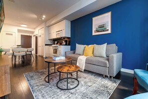 A modern living room with a grey sofa, a coffee table, and a blue accent wall. - Stylish 2BR City Retreat Near the Lake & Park (Toronto)