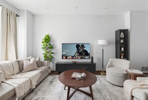 Ein modernes Wohnzimmer mit einer Couch, einem Sessel, einem Couchtisch und einem flachbildfernseher an der Wand.