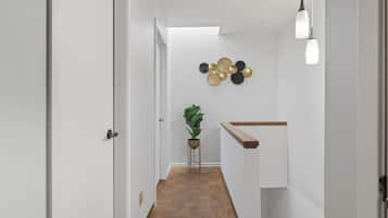 A hallway with a wooden floor, white walls, a plant, and a wall-mounted light fixture.
