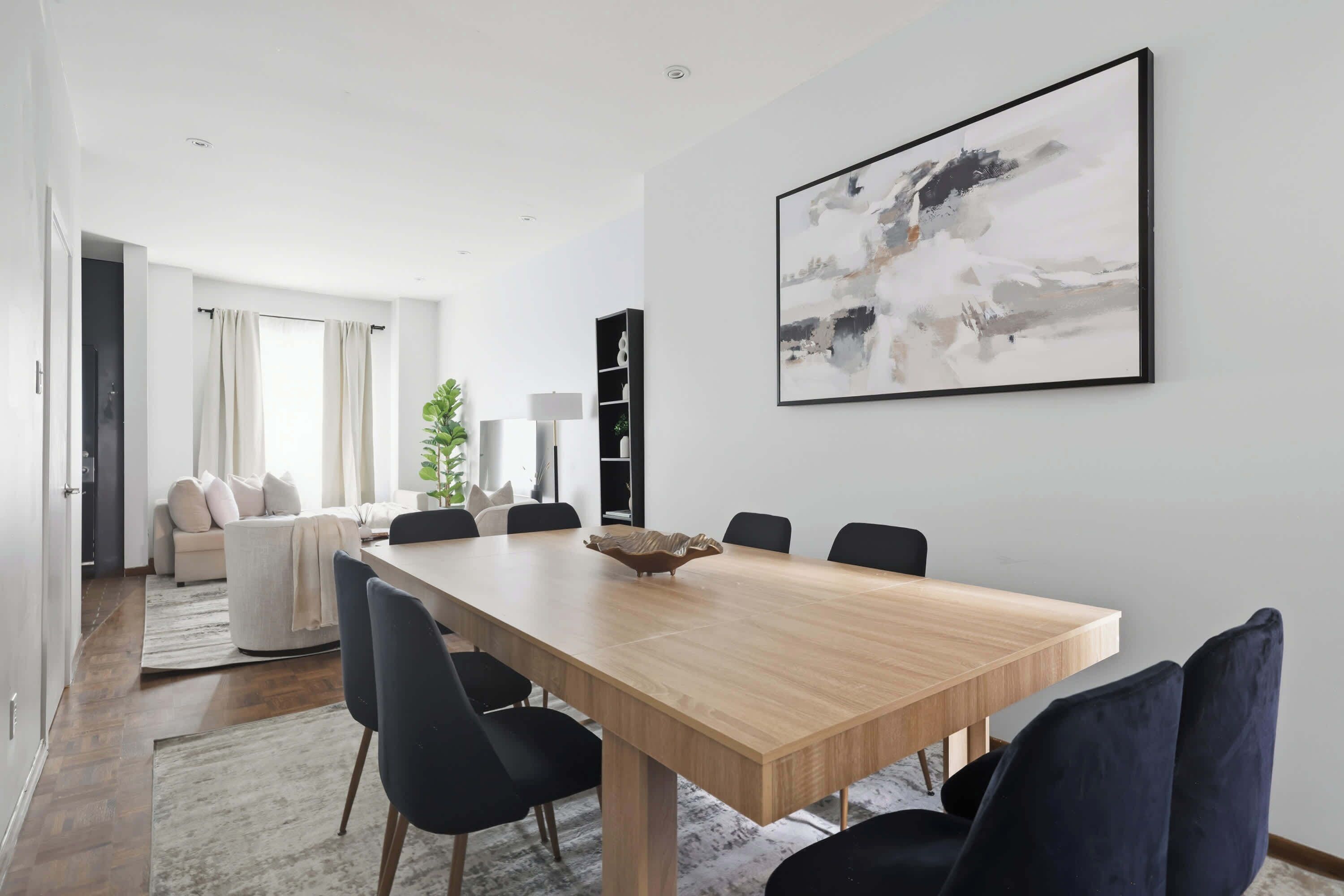 A modern dining area with a wooden table, black chairs, and a large abstract painting on the wall.