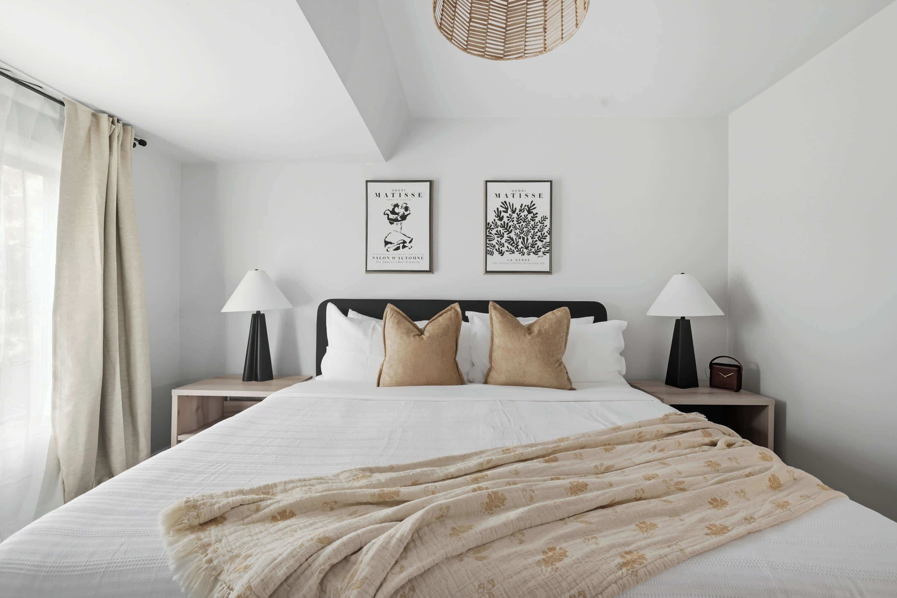 A hotel room with a bed, two nightstands, a lamp, a framed artwork, and a window with curtains.