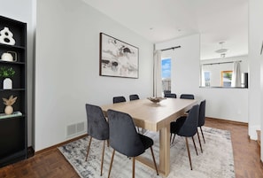 Ein stilvolles Esszimmer mit einem Holztisch, schwarzen Stühlen, einem weißen Teppich und einem Gemälde an der Wand.