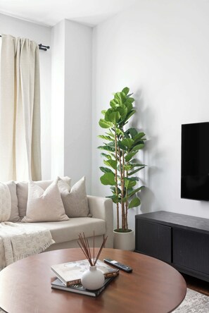 A modern living room with a sofa, a coffee table, a plant, and a TV. - Grand 4BR Downtown Townhome escapade (Toronto)