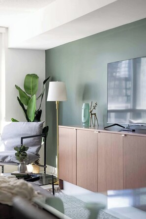 A modern living room with a sofa, a television, a cabinet, a lamp, and a plant. - Modern 2BR Waterfront Retreat City Views | Parking Available (Toronto)