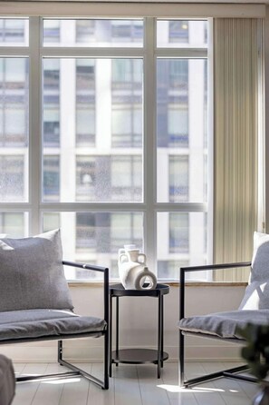 Ein Zimmer mit großem Fenster, zwei Stühlen, einem kleinen Tisch und einer Vase.