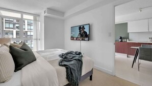 Un dormitorio moderno con una cama grande, un televisor instalado en la pared y vistas de la ciudad a través de la ventana.