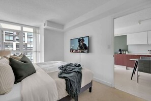 Ein modernes Schlafzimmer mit einem großen Bett, einem an der Wand befestigten Fernseher und Blick auf die Stadt durch das Fenster.