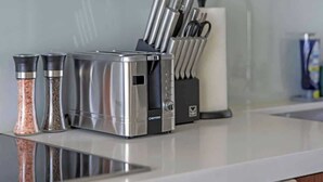 Una encimera de cocina con un tostador, saleros y pimenteros, un bloque de cuchillos y un rollo de toallas de papel.