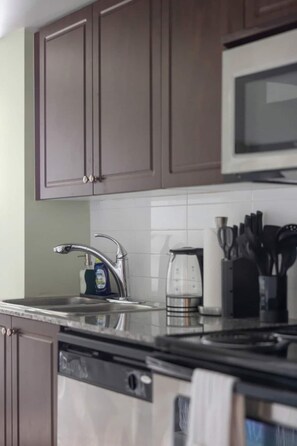 A kitchen with a stainless steel dishwasher, a kettle, a microwave, and a knife block.