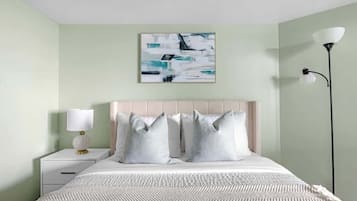 Quarto com cama, mesa de cabeceira, luminária e obra de arte na parede.