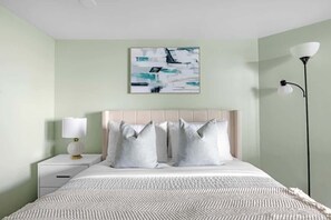 Une chambre à coucher comprenant un lit, une table de chevet, une lampe et une œuvre d’art accrochée au mur.
