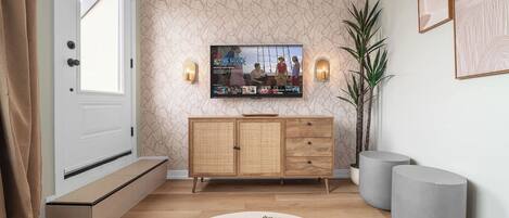 Un salon moderne avec un téléviseur fixé au mur, un meuble en bois, une plante en pot et une table basse ronde.