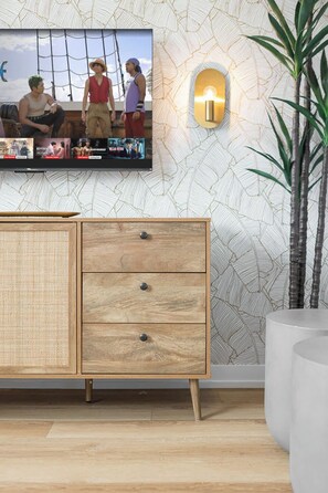 Ein Zimmer mit einem an der Wand befestigten Fernseher, einem Holzkasten mit Schubladen und einem Blumentopf.