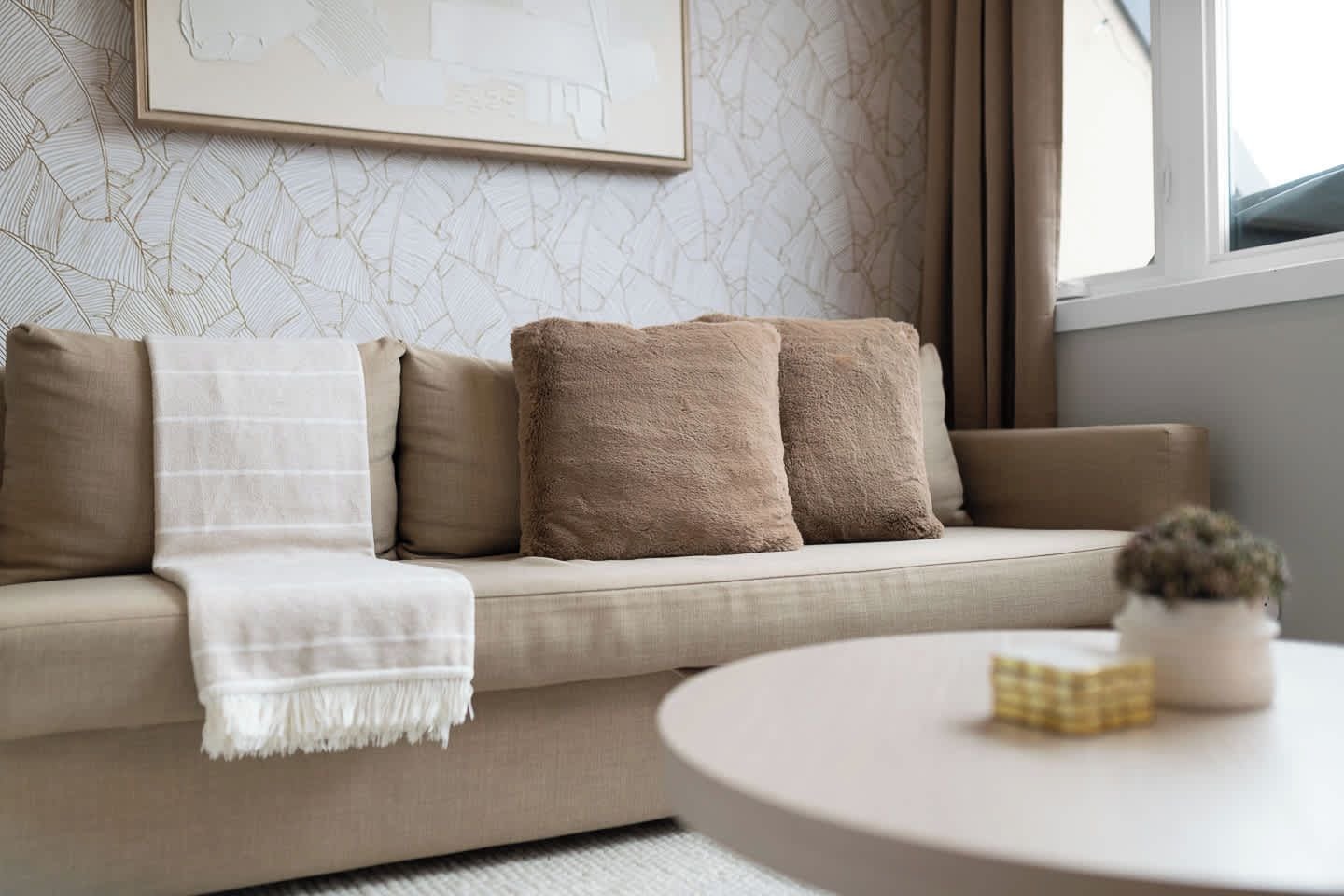 A modern living room with a sofa, pillows, a throw blanket, and a small table with a plant.
