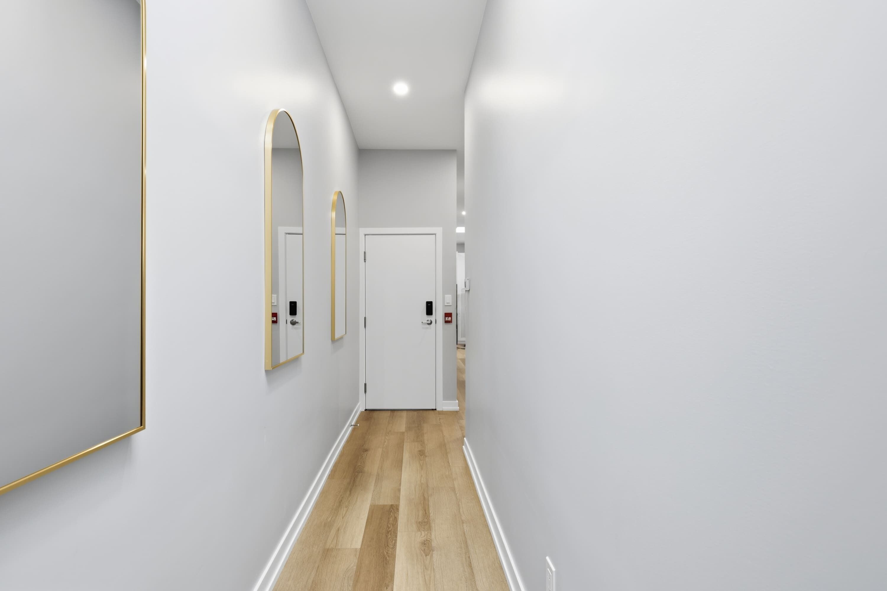 A hallway with white walls, a wooden floor, and a door at the end.