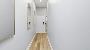 A hallway with white walls, a wooden floor, and a door at the end. - Rare 3BR Gem, Mini Putt Terrace & CN Tower Views! (Toronto)