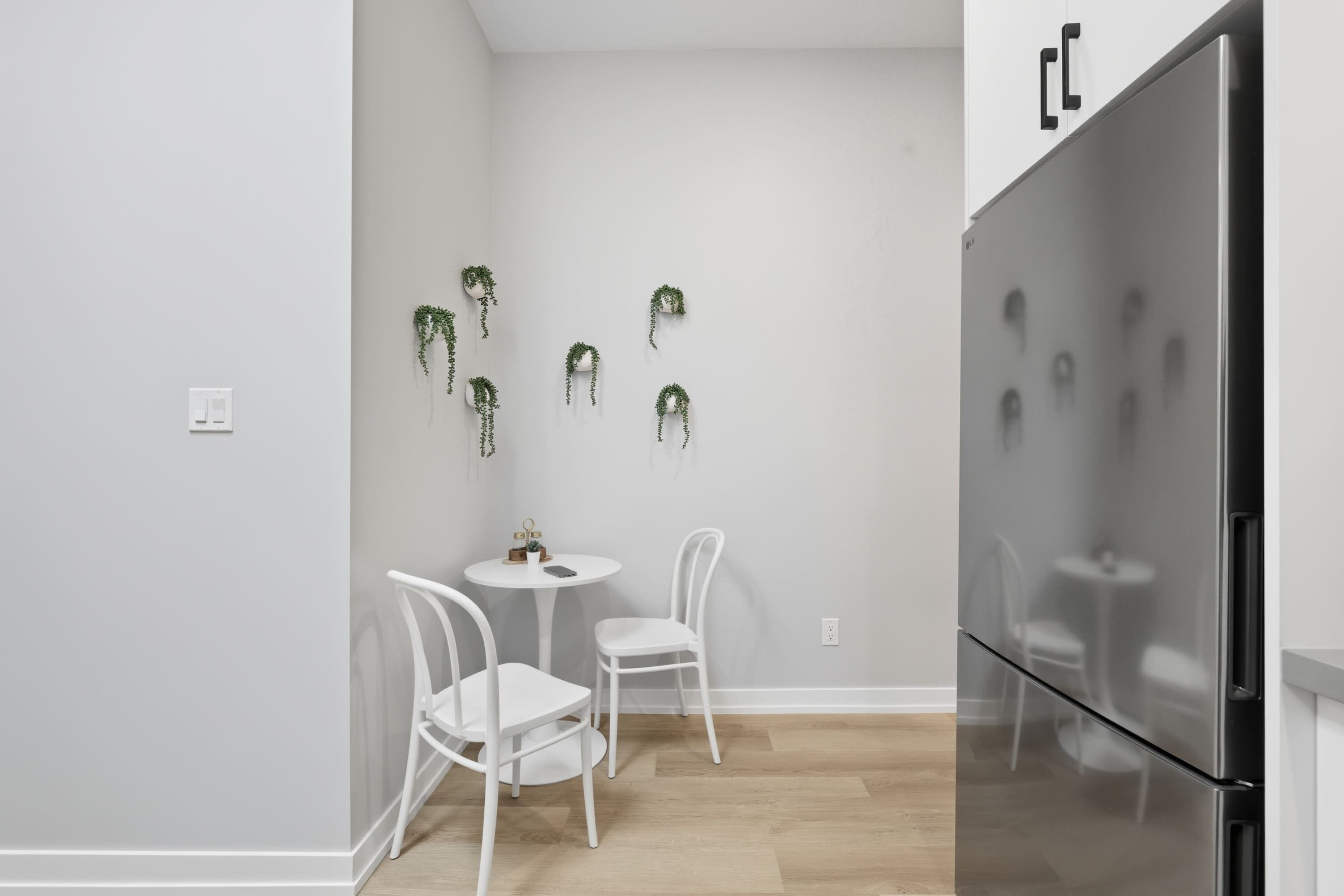 A modern kitchen with a stainless steel refrigerator, two white chairs, and a small round table with a potted plant.