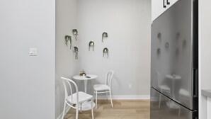 A modern kitchen with a stainless steel refrigerator, two white chairs, and a small round table with a potted plant. - Rare 3BR Gem, Mini Putt Terrace & CN Tower Views! (Toronto)
