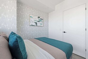 A bedroom with a bed, pillows, a wall-mounted artwork, and a door. - Modern 2BR Retreat with Private Balcony & Parking (Toronto)