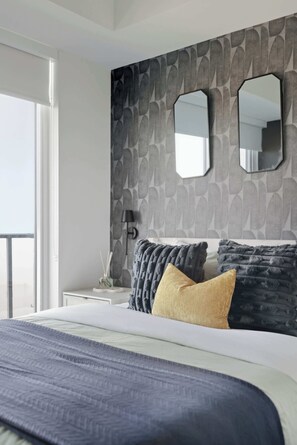 A modern bedroom with a large bed, a nightstand, a lamp, and a window. - Modern 2BR Retreat with Private Balcony & Parking (Toronto)