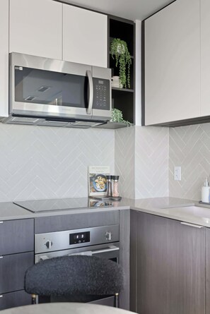 Una cocina moderna con un microondas de acero inoxidable, un horno empotrado y un pequeño comedor con una silla.