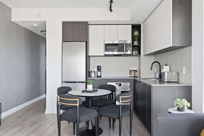 A modern kitchen with a central island, built-in appliances, and a dining area with a round table and chairs. - Modern 2BR Retreat with Private Balcony & Parking (Toronto)