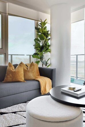 A modern living room with a grey sofa, a round coffee table, and a large window offering a view of the outdoors. - Modern 2BR Retreat with Private Balcony & Parking (Toronto)