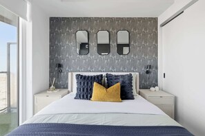 A modern bedroom with a large bed, a nightstand with a lamp, and a wall with three mirrors.