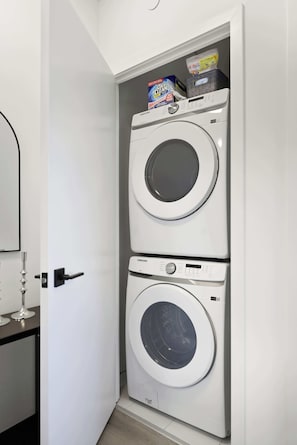 Un cuarto de lavandería con dos lavadoras apiladas y una caja de OxiClean encima.