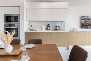 A modern kitchen with a central island, a dining area with a wooden table, and a painting on the wall. - CityPlace 2BR Escape | Balcony & 2 Bathrooms (Toronto)