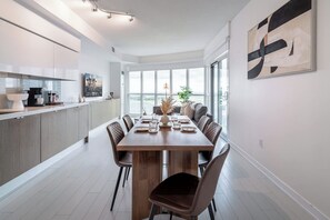 A modern kitchen with built-in appliances, a dining area with a long wooden table, and a large window providing a view of the outdoors. - CityPlace 2BR Escape | Balcony & 2 Bathrooms (Toronto)