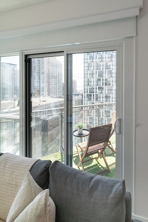Ein Balkon mit Blick auf hohe Gebäude, ein kleiner Tisch mit einer Pflanze und ein Holzstuhl.