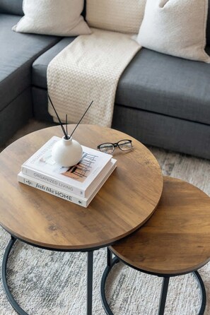 A round wooden coffee table with a white vase and books, placed on a carpeted floor.