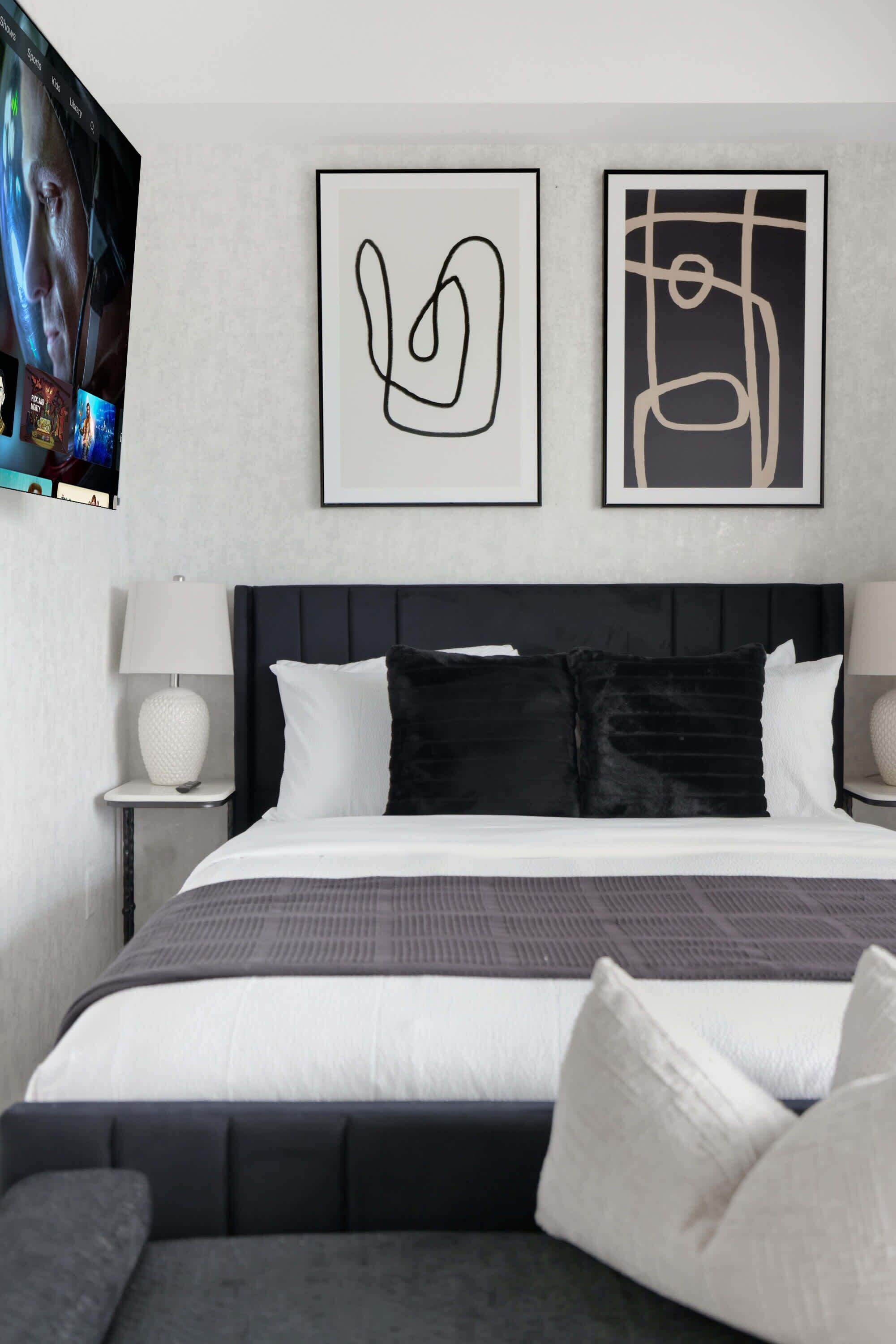 Ein modernes Schlafzimmer mit einem Bett, Kissen und zwei an der Wand befestigten Kunstwerken.