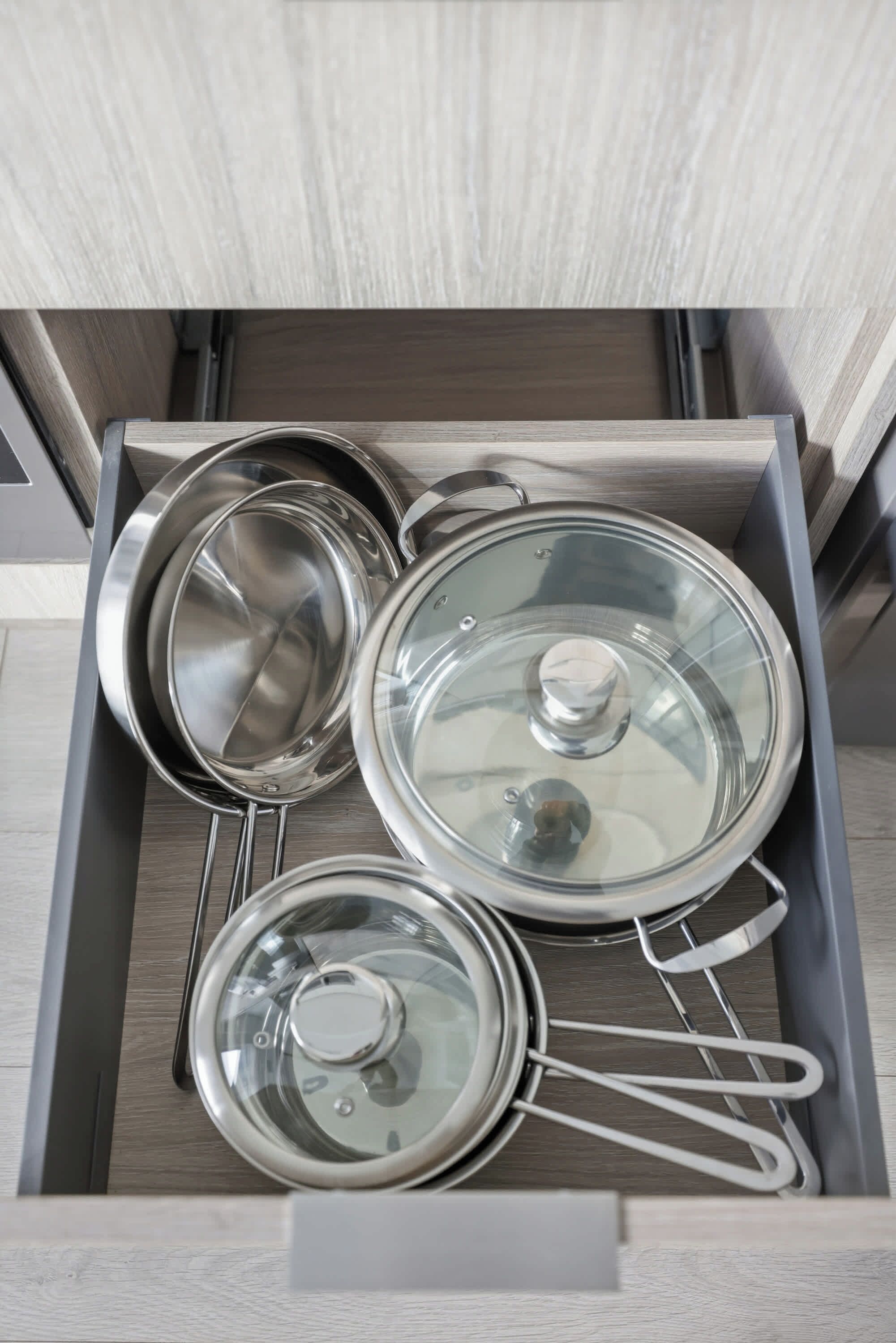 A drawer with stainless steel kitchenware including pots and pans.