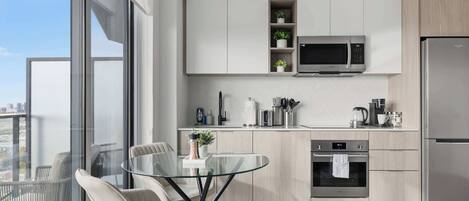 A modern kitchen with a glass dining table, stainless steel appliances, and a view of the city.