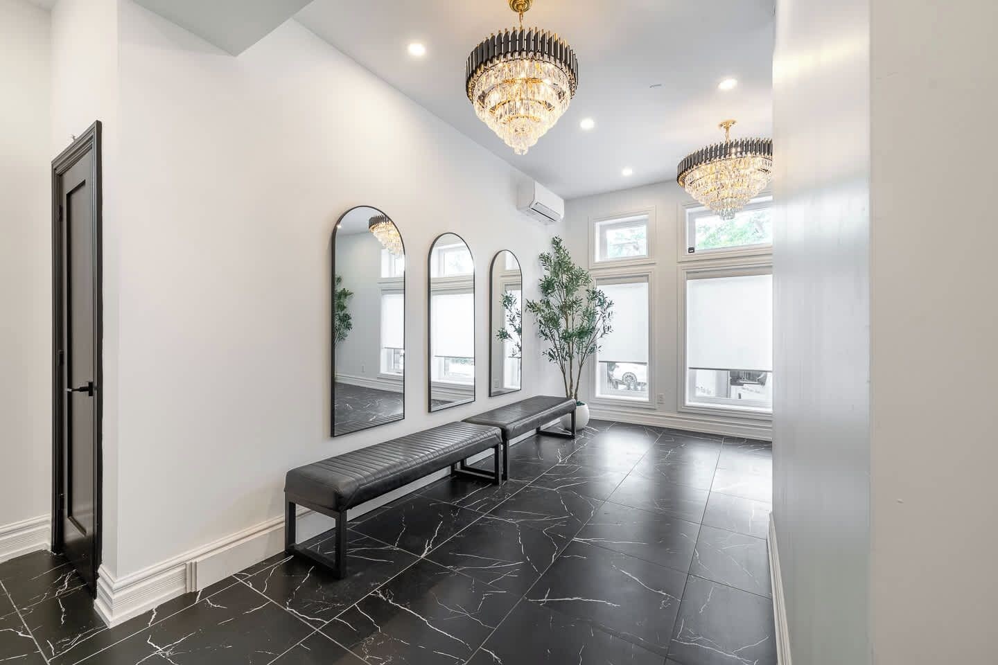 A hallway with a bench, three mirrors, and two chandeliers.