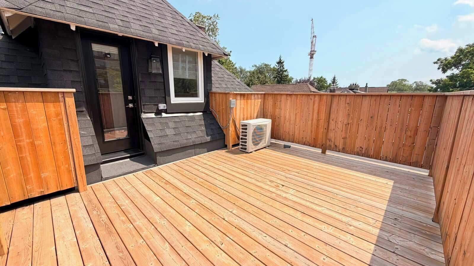 Een houten terras met een klein gebouw, een raam en een airconditioning.