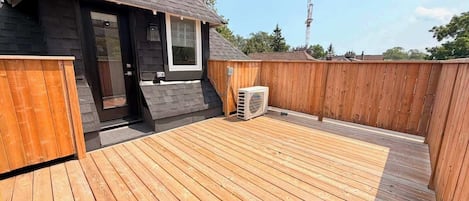 Een houten terras met een klein gebouw, een raam en een airconditioning.