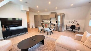 Ein modernes Wohnzimmer mit Flachbildfernseher, Essbereich, Küche inklusive Edelstahlkühlschrank und Arbeitsbereich mit Schreibtisch und Stuhl.