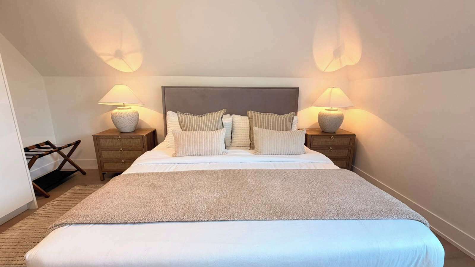 Une chambre d’hôtel avec un grand lit, deux tables de chevet avec des lampes et un petit coin salon avec un fauteuil.