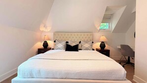 Ein Schlafzimmer mit einem großen Bett, zwei Nachttischen mit Lampen, einem grauen Bürostuhl und einer schrägen Decke mit Dachfenster.