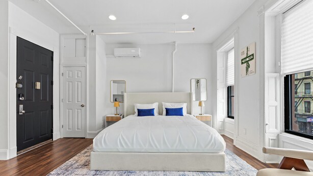 A hotel room with a large bed, a window with a view, a door, and an air conditioning unit.