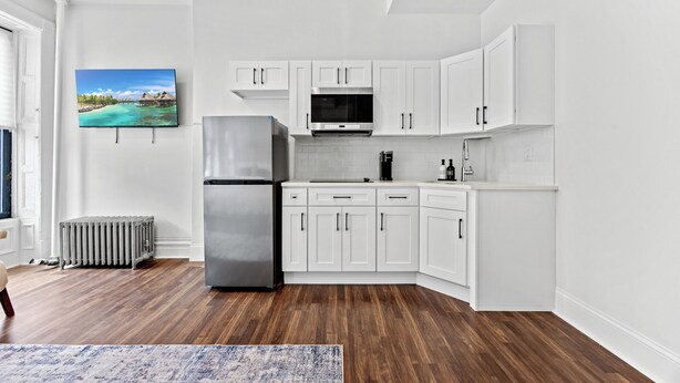 A modern kitchen with white cabinets, a stainless steel refrigerator, a microwave, and a coffee maker.