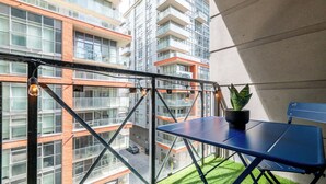Uma varanda com uma mesa azul, um vaso de planta e vista para um edifício alto.