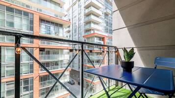 Un balcon avec une table bleue, un pot de fleurs et une vue sur un immeuble à plusieurs étages.