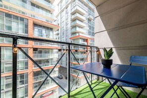 Ein Balkon mit blauem Tisch, einem Blumentopf und Blick auf ein mehrgeschossiges Gebäude.