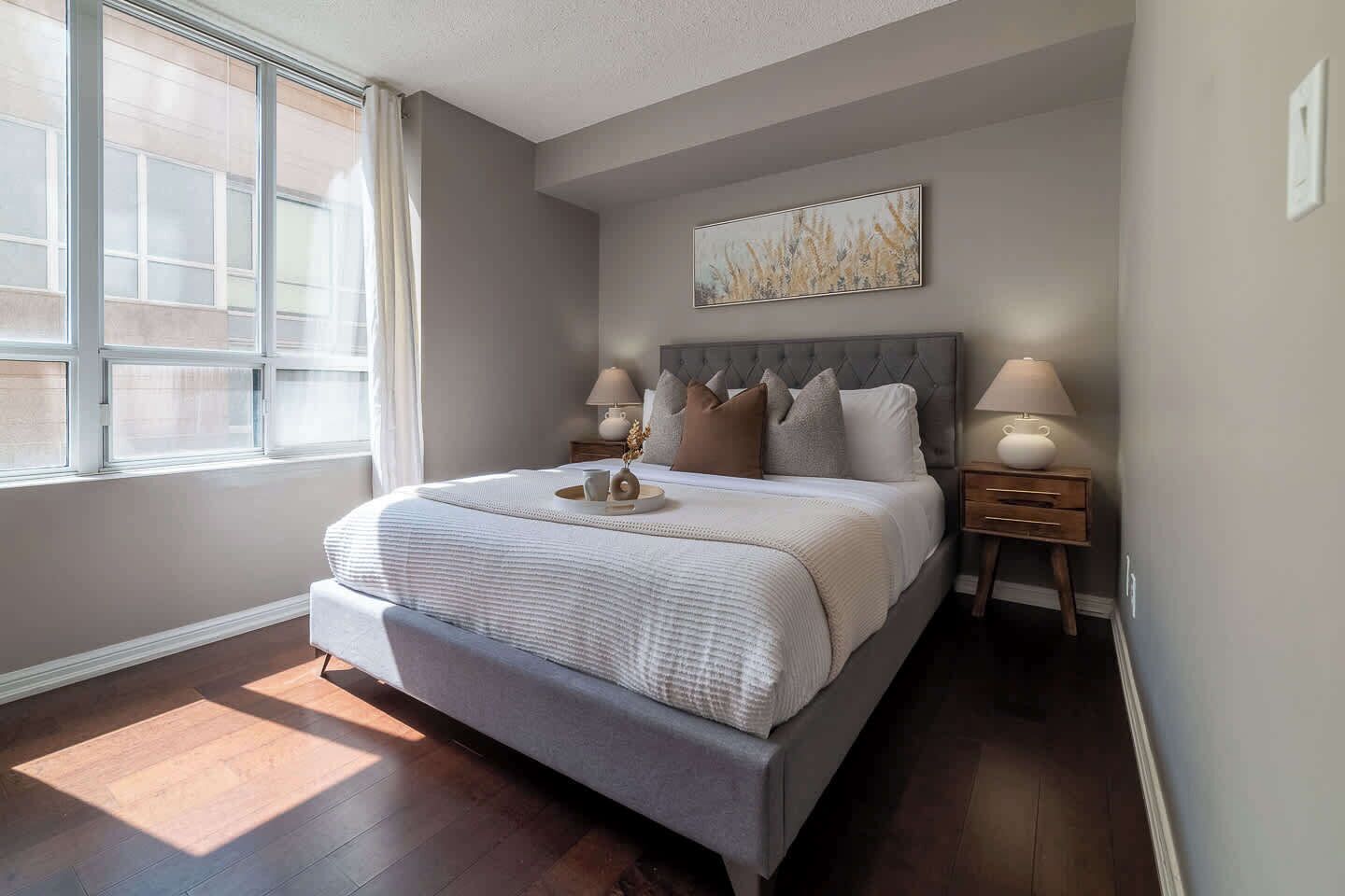 A bedroom with a large bed, bedside tables, a window, and a painting on the wall.
